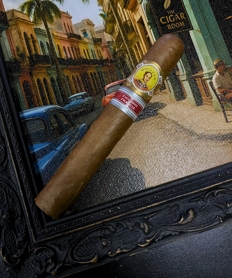 Cigar with a label in front of a framed picture of a street scene. Bolívar Libertador Regional Edition France 