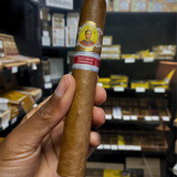 Cigar held by a hand with shelves of cigars in the background. Bolívar Libertador Regional Edition France 