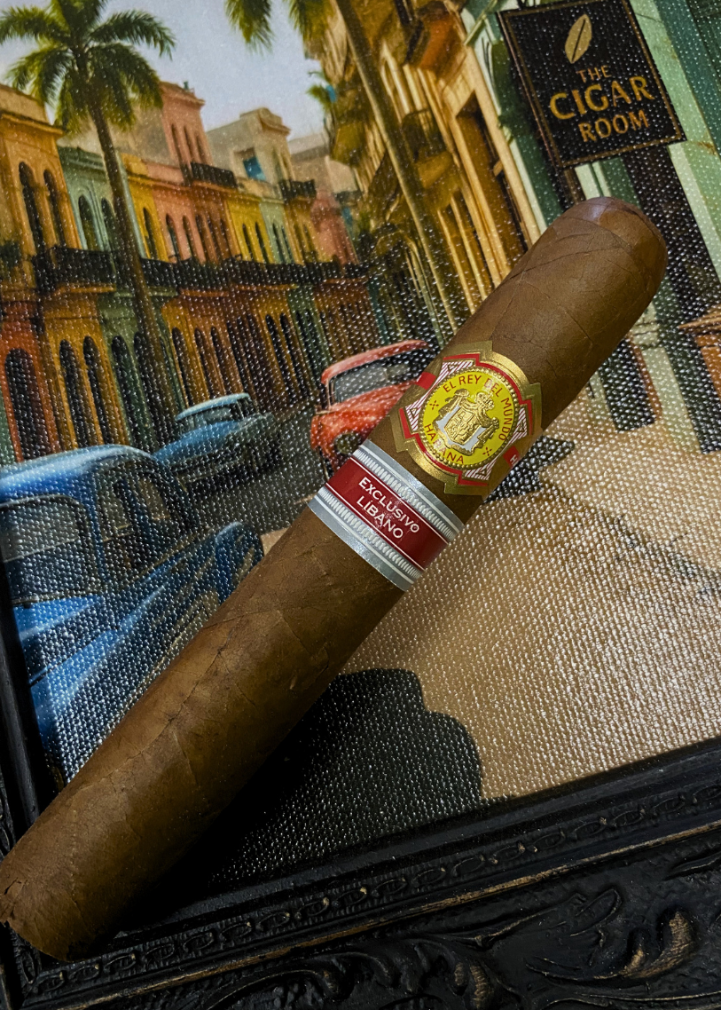 Cigar with a visible label on a textured surface, with a colorful cityscape in the background. El Rey del Mundo W.I.H. 20 Years Regional Edition Lebanon 
