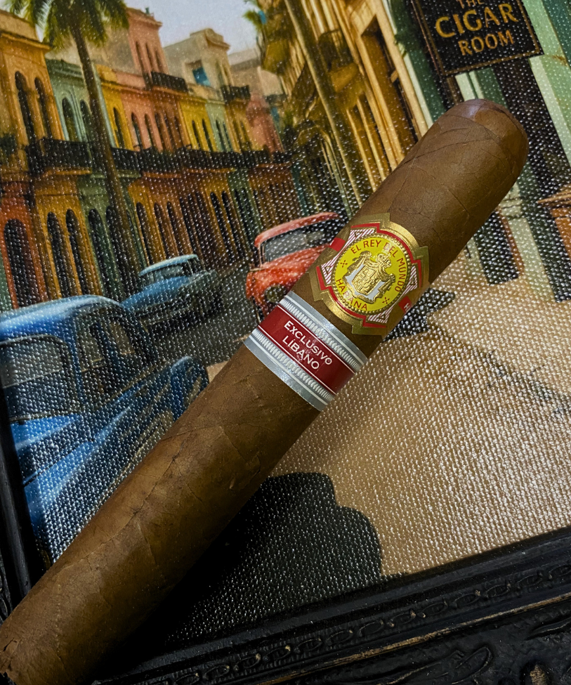 Cigar with a visible label on a textured surface, with a colorful cityscape in the background. El Rey del Mundo W.I.H. 20 Years Regional Edition Lebanon 