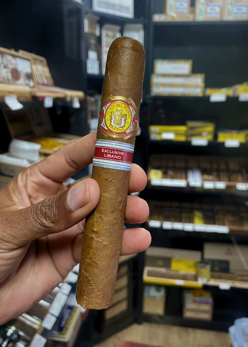 Cigar held by a hand with a blurred store shelf in the background. El Rey del Mundo W.I.H. 20 Years Regional Edition Lebanon 