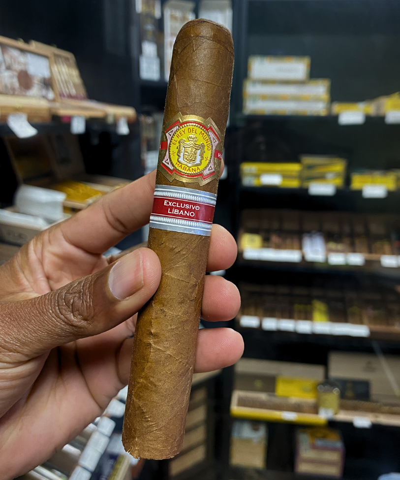Cigar held by a hand with a blurred store shelf in the background. El Rey del Mundo W.I.H. 20 Years Regional Edition Lebanon 