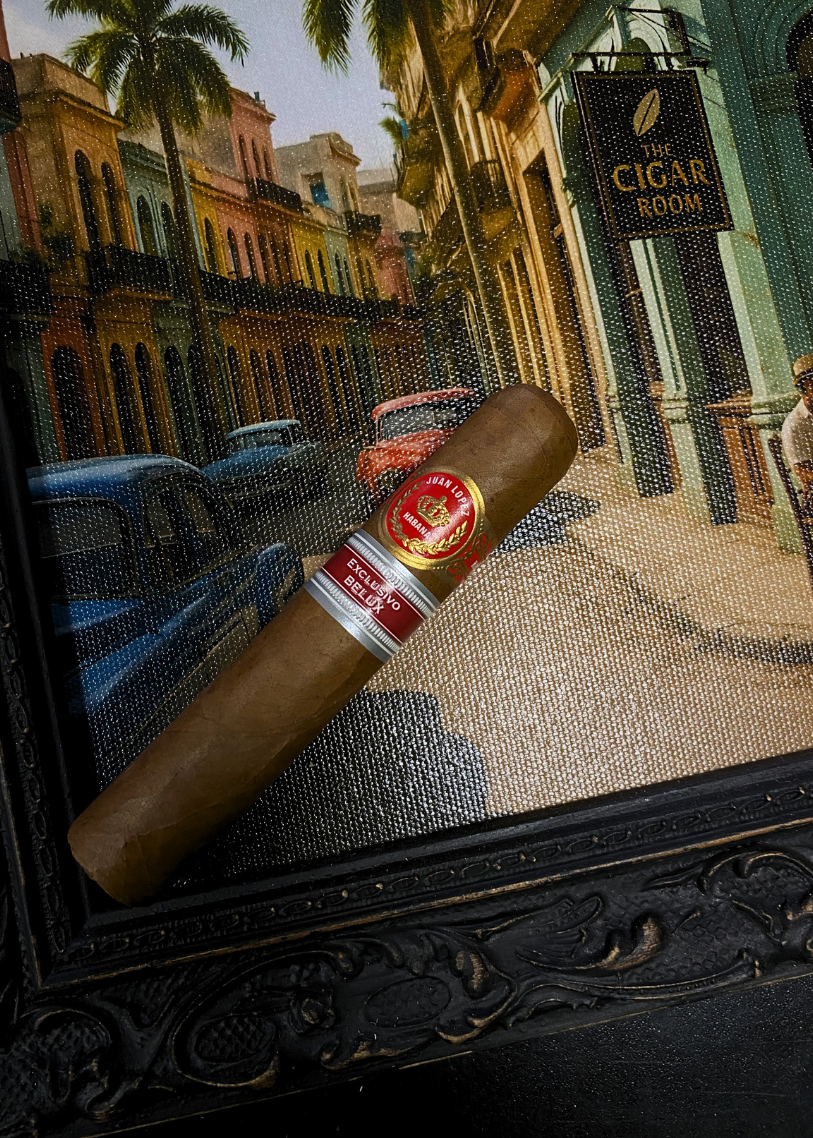 Cigar with a brand label on a decorative mat featuring a street scene with palm trees and buildings.