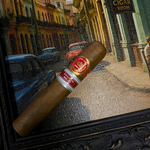 Cigar with a brand label on a decorative mat featuring a street scene with palm trees and buildings.