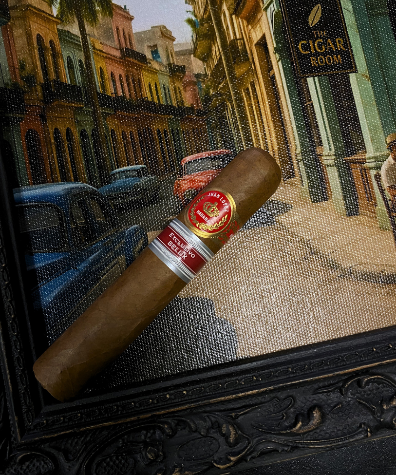 Cigar with a brand label on a decorative mat featuring a street scene with palm trees and buildings.