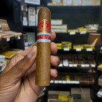 Hand holding a cigar with a brand label in a store setting