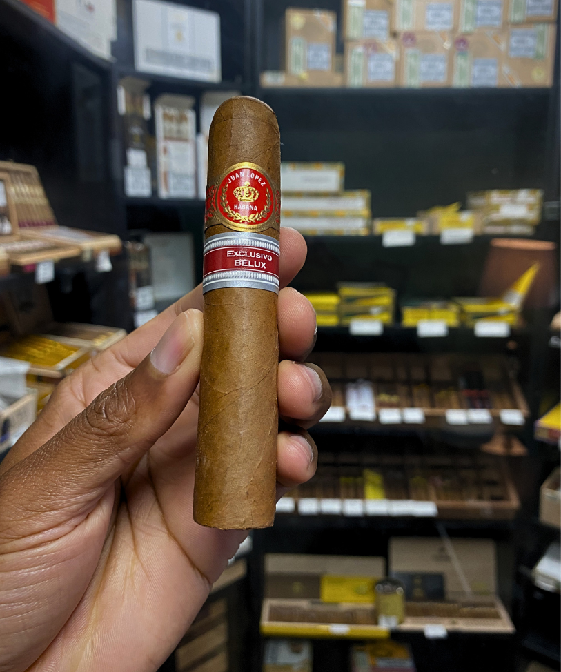 Hand holding a cigar with a brand label in a store setting
