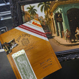 Cigar box with Habano and Juan Lopez branding in front of a painting of a street scene.
