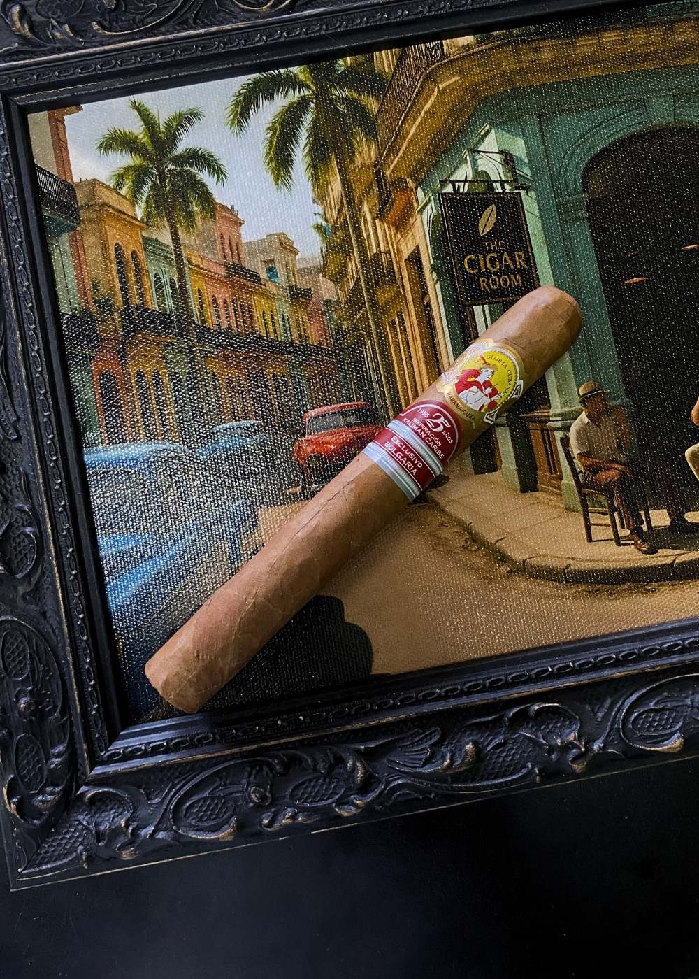 Cigar with a 'Vitello' label in front of a framed painting of a street scene.