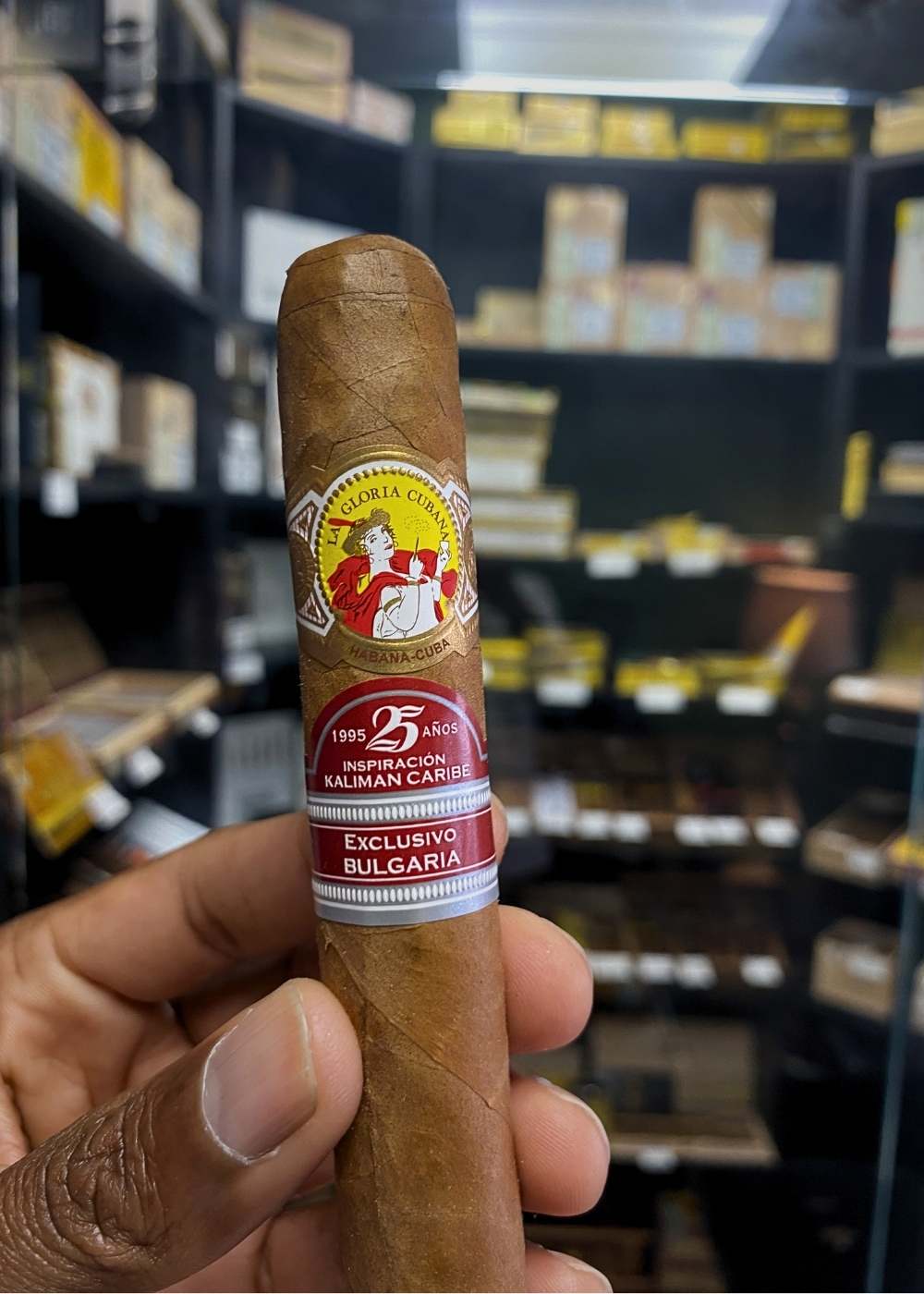 Cigar with a visible label held in front of a shelf with more cigars.