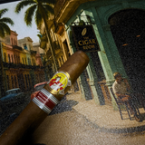 Cigar with band held over a painting of a street scene with 'The Cigar Room' sign.