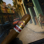Cigar with a label held in front of a decorative background featuring a sign for 'The Cigar Room'. Ramón Allones Caprichos Regional Edition Spain