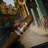 Cigar with a label held in front of a decorative background featuring a sign for 'The Cigar Room'. Ramón Allones Caprichos Regional Edition Spain