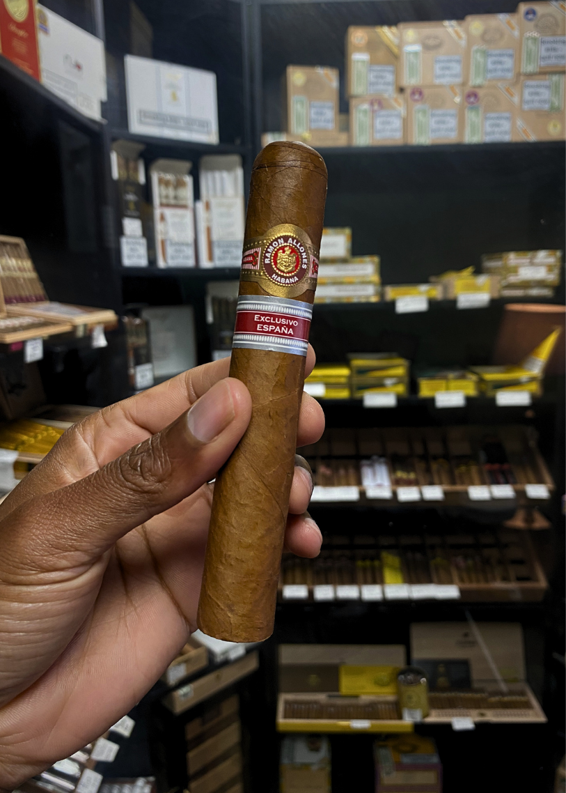 Hand holding a cigar with a brand label in a store setting. Ramón Allones Caprichos Regional Edition Spain