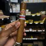 Hand holding a cigar with a brand label in a store setting. Ramón Allones Caprichos Regional Edition Spain
