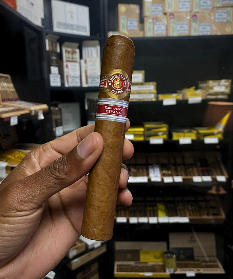 Hand holding a cigar with a brand label in a store setting. Ramón Allones Caprichos Regional Edition Spain