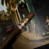 Cigar with a band in front of a mosaic wall featuring a cigar store sign. Ramón Allones Grandes Regional Edition Spain