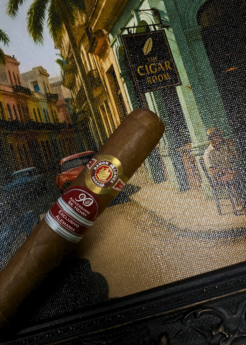 Cigar with a brand label on a decorative surface featuring a painting of a street scene. Ramón Allones Sr. Henry Regional Edition Germany 2020 