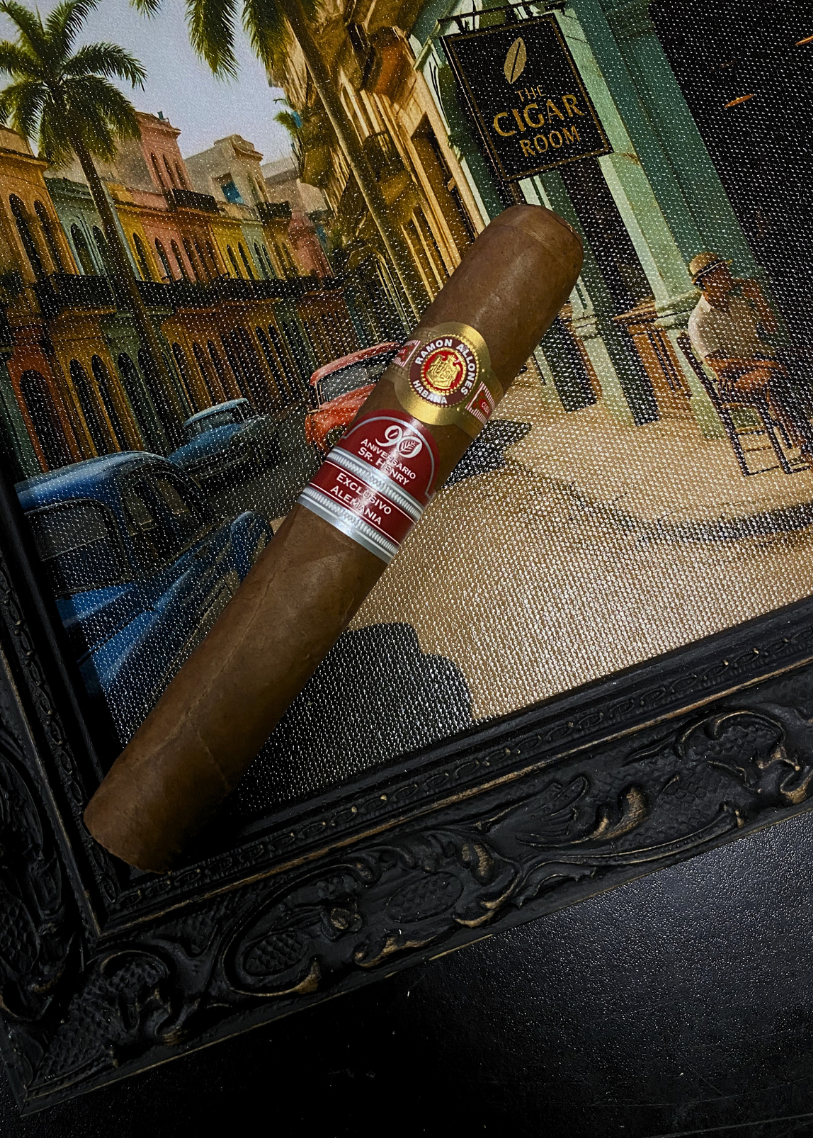 Cigar with a brand label in front of a painting of a city street scene. Ramón Allones Sr. Henry Regional Edition Germany 2020 