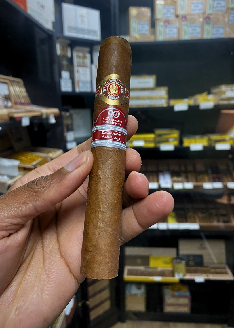Cigar held in a hand with a blurred store shelf in the background. Ramón Allones Sr. Henry Regional Edition Germany 2020 