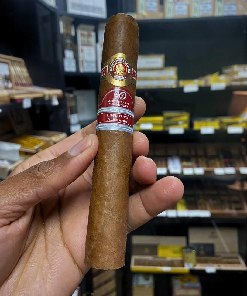 Cigar held in a hand with a blurred store shelf in the background. Ramón Allones Sr. Henry Regional Edition Germany 2020 