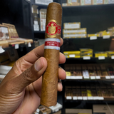Cigar held by a hand with shelves of cigars in the background. Saint Luis Rey Marquéz Regional Edition Exclusive Cuba 2016