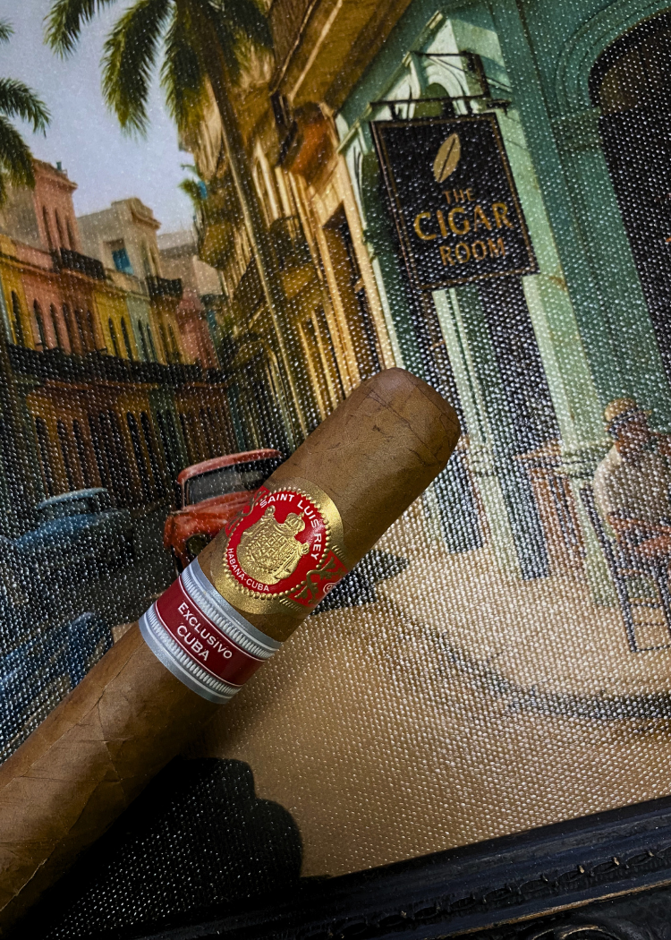 Cigar with a red band in front of a painting of a street scene. Saint Luis Rey Marquéz Regional Edition Exclusive Cuba 2016