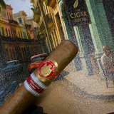 Cigar with a red band in front of a painting of a street scene. Saint Luis Rey Marquéz Regional Edition Exclusive Cuba 2016