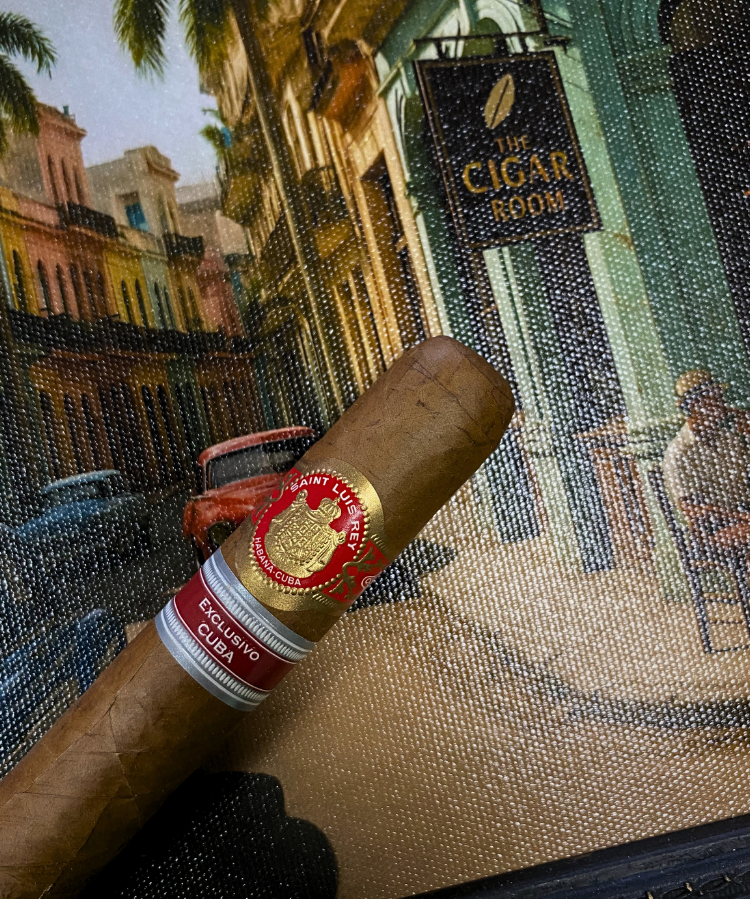 Cigar with a red band in front of a painting of a street scene. Saint Luis Rey Marquéz Regional Edition Exclusive Cuba 2016
