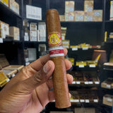 Cigar held in a hand with a blurred background of shelves with cigars