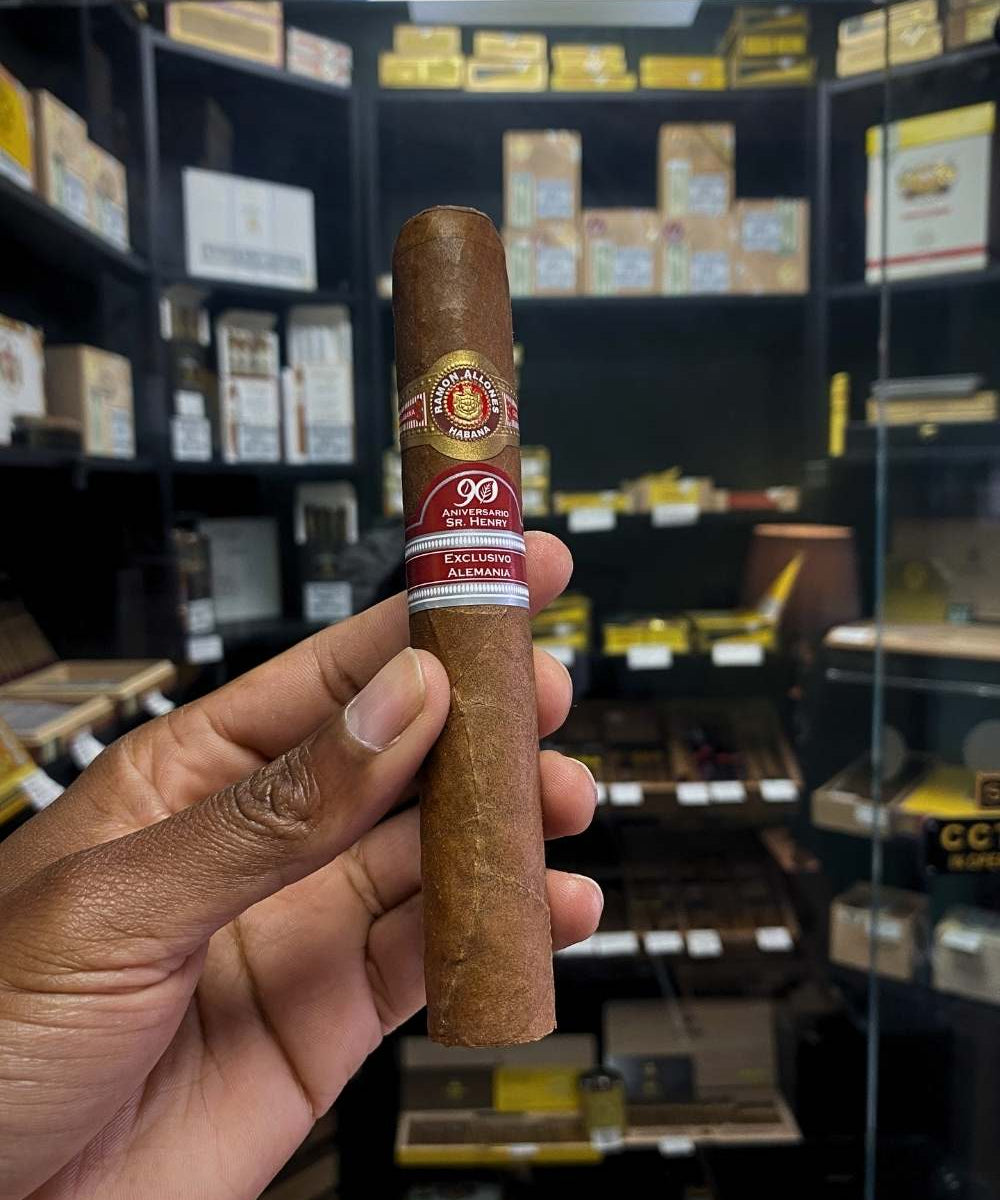 Cigar held by a hand with a store shelf of cigars in the background